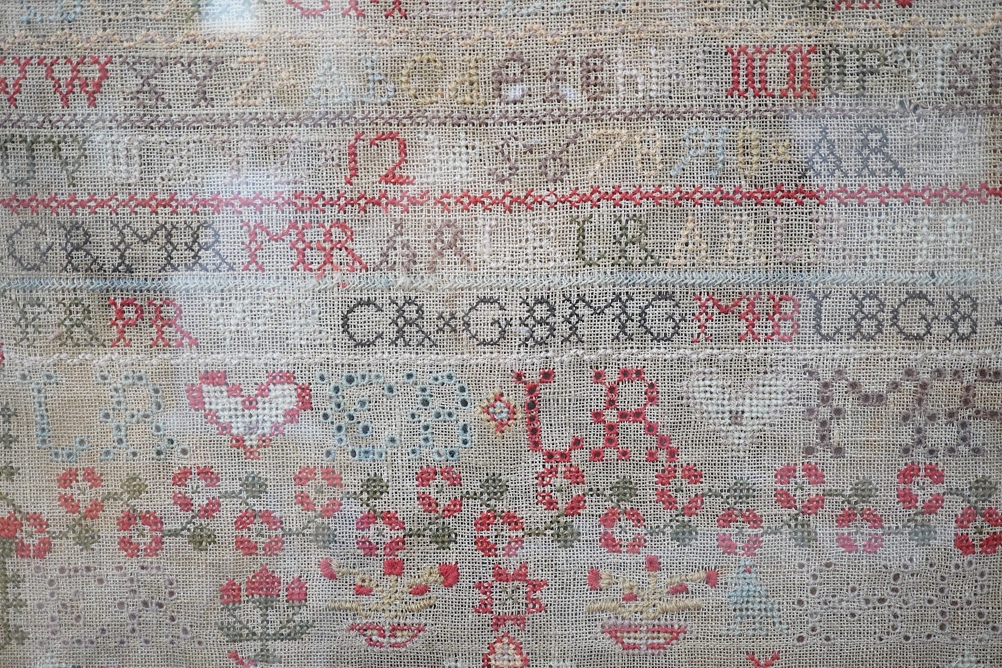 A large framed cross stitch sampler, by Helen Rae, dated 1851, worked mostly in red and green, with an ornate floral border around alphabet letters and numerals, large button hole letters and motifs, with a large central